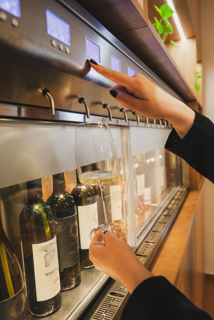 Ruka stláčajúca tlačidlo na enomate, samoobslužnom výdajníku vína.