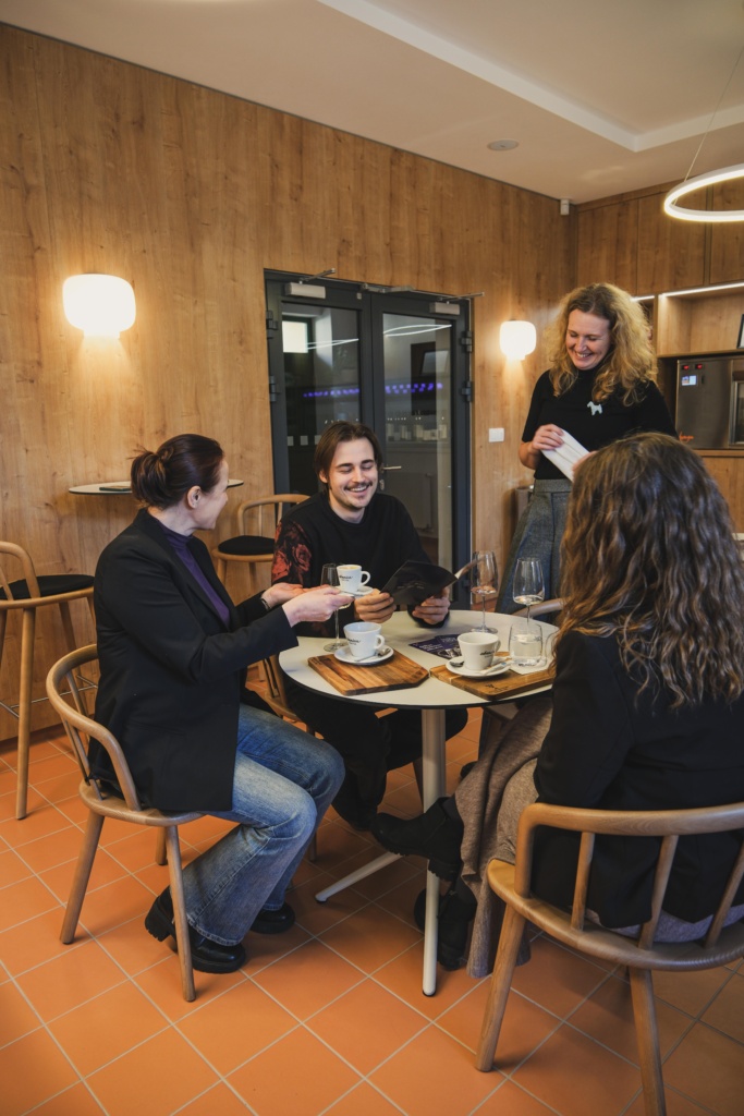 Muž, dve ženy jedna strašia, jedna mladšia sedia vo vinotéke a someliérka im prezentuje ponuku.